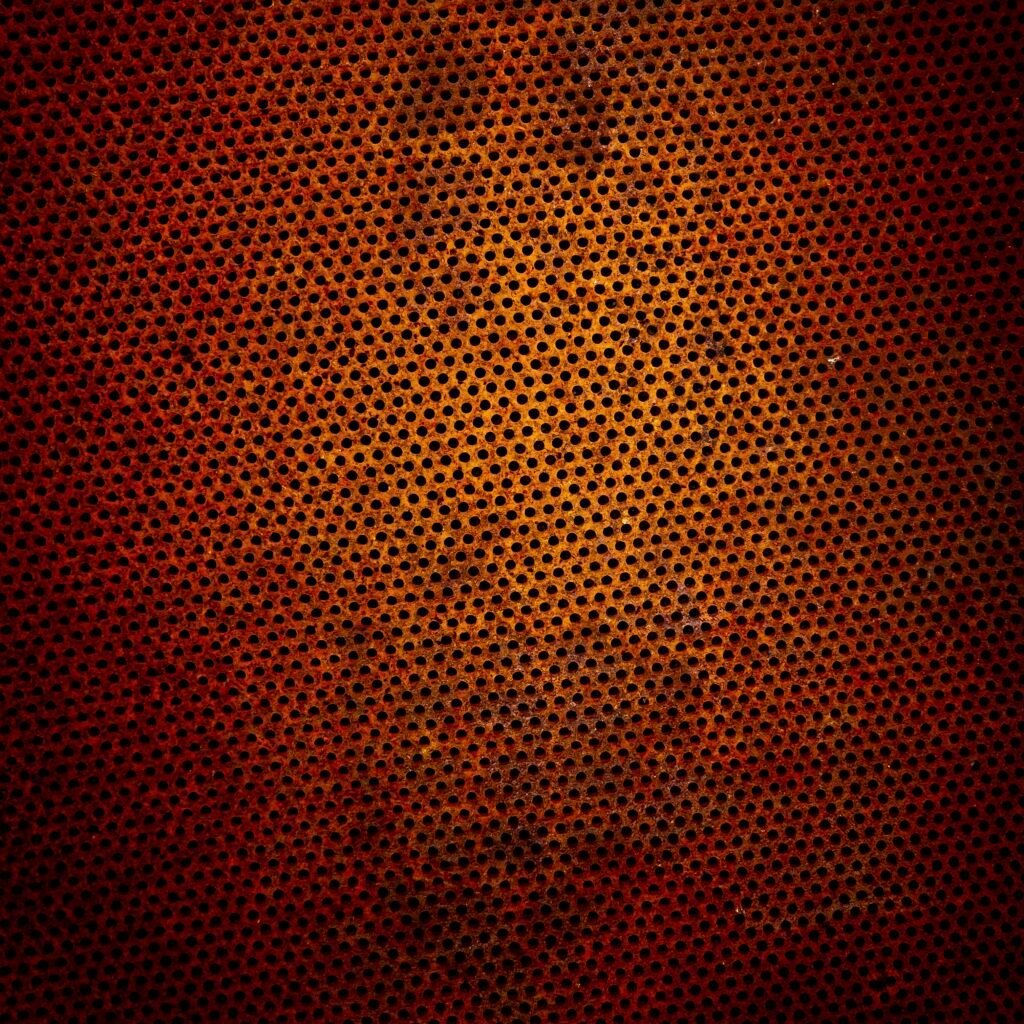 Abstract close-up of rusty perforated metal with orange-brown patina and grid of round holes, evoking industrial decay and time’s erosion.
